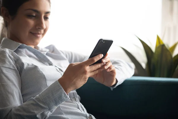 Indian woman relaxing on comfy sofa with smartphone closeup image