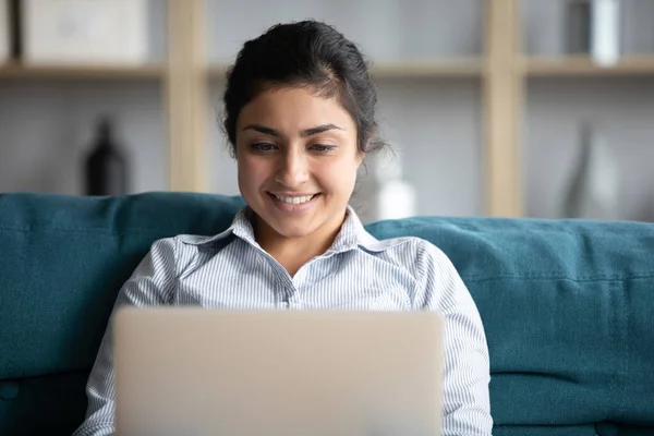 Indian girl using laptop seated on comfy couch at home — Stock Photo, Image