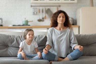 Huzurlu genç anne ve küçük kız meditasyon yapıyor, yoga yapıyor.