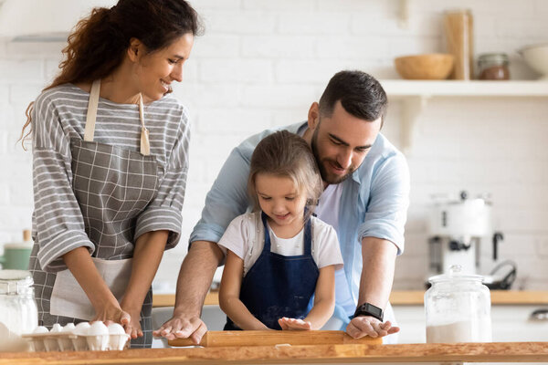 Caring father teaching little daughter to work rolling pin