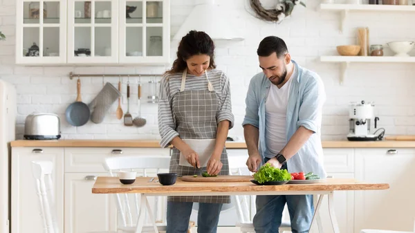 Happy young couple preparing salad in modern kitchen together — Stock Photo, Image