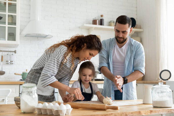 Happy parents and adorable little daughter cooking dough together