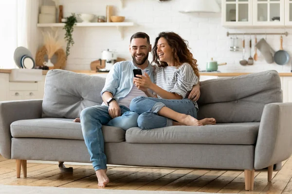 Glückliche junge Frau und Mann, die sich umarmen und gemeinsam das Smartphone benutzen — Stockfoto