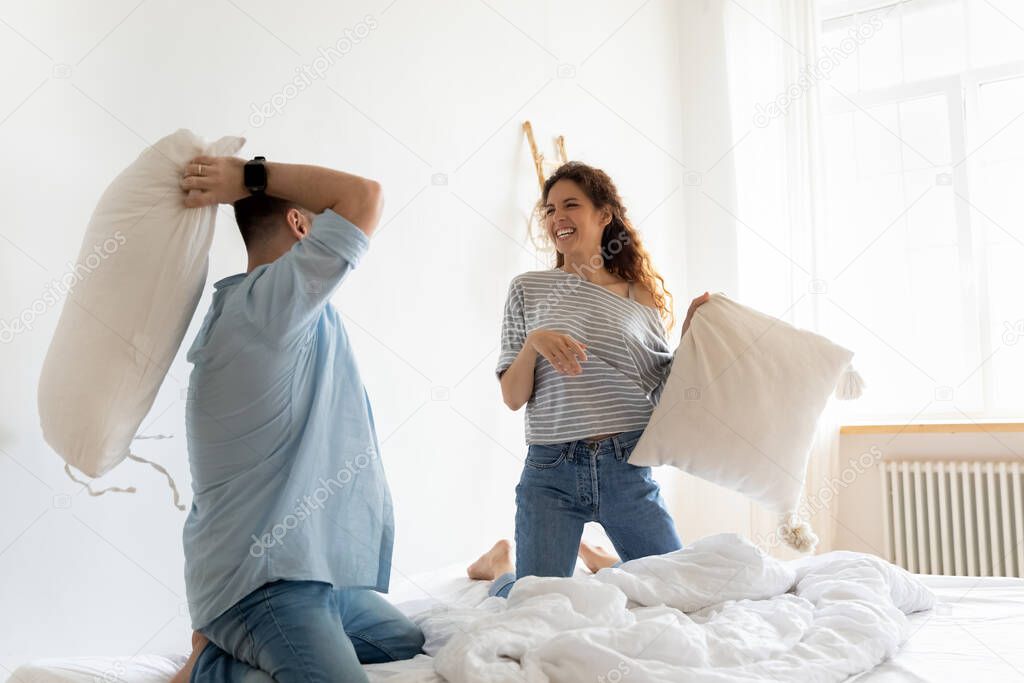 Happy laughing young couple playing pillow fight in bedroom