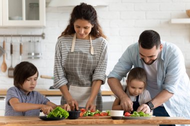 İki çocuklu mutlu bir aile salata pişiriyor, sebze kesiyor.