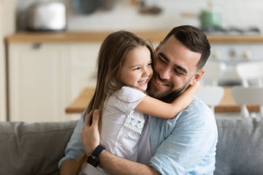 Gülümseyen genç bir baba, sevimli bir kıza sarılıyor.