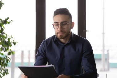 Kağıt belgeye bakan odaklı genç Arap etnik köken erkek yönetici.