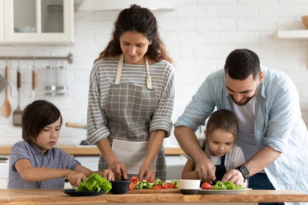 Gelukkig gezin met twee kleine kinderen koken salade, snijden van groenten — Stockfoto