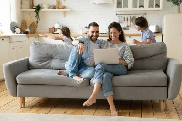 Glückliche Eltern mit Laptop, während Kinder lustiges Spiel spielen — Stockfoto