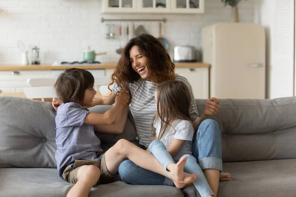Веселая мать, развлекающаяся с двумя детьми дома, щекочущая — стоковое фото