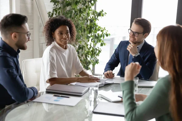 Glückliche multiethnische Geschäftsleute, die ihrem afrikanisch-amerikanischen Kollegen zuhören. — Stockfoto