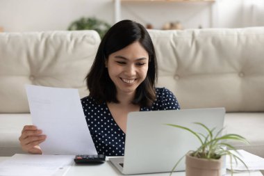 Gülümseyen Asyalı kadın faturalarını laptoptaki kolay bankacılıkla ödüyor.