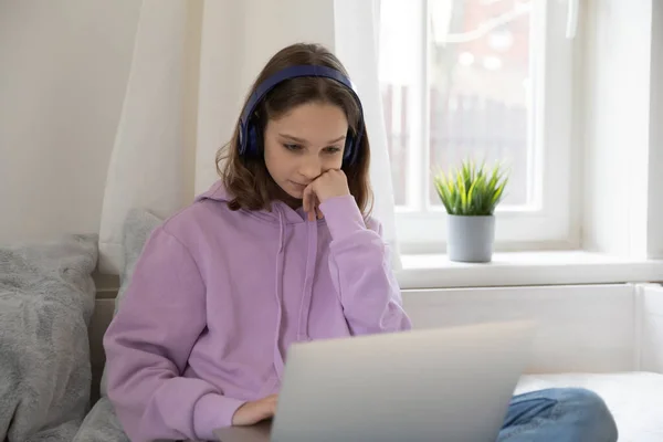 Pensive teen girl in headphones using laptop at home — Stock Photo, Image
