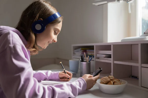 Smiling teen girl in headphones study at home using cellphone — Stock Photo, Image