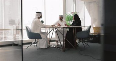 Üç genç erkek ve kadın Arap hissedarlardan oluşan bir grup büyük masada şirketi tartışıyor, başarılı bir başlangıç projesine yatırım yapmayı planlıyor, ofis kapısındaki toplantı masasında konuşuyor.