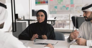 Gözlüklü genç Müslüman iş kadını, siyah tesettür ve abaya toplantı masasında meslektaşlarına beyin fırtınası, etkili takım çalışması yönetimi fikirleri sunuyorlar.