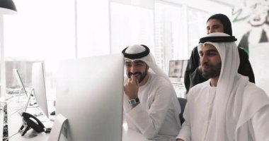 Üç mutlu Arap ofis arkadaşından oluşan ekip masaüstü monitöründe komik videolar izliyor, online ürünü tartışıyor ve analiz ediyor, ekranı gösteriyor, konuşuyor, gülümsüyor, gülüyor.,