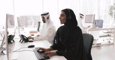 Genç bayan Arap çağrı merkezi çalışanı mikrofon ile bilgisayar monitöründe ses çağrısı yapan, klavyede yazan, teknik destek veren,