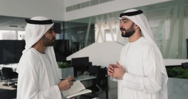 Beyaz geleneksel elbiseli, takım çalışması, ağ kurma, iş molasında sohbet etme ve çevrimdışı profesyonel iletişimden keyif alma konularını tartışan iki Arap erkek iş arkadaşı.