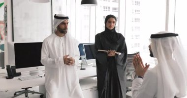 Müslüman elbiseli üç erkek ve kadın Arap işadamı ofiste çalışma stratejilerini tartışıyor, daireler çiziyor, konuşuyor, görevler planlıyor, yarışıyor, yaratıcı fikirler üzerinde kafa patlatıyor.