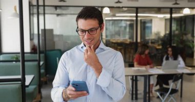 Pozitif İtalyan işadamı, girişimci ya da erkek ofis çalışanı birlikte çalışma alanındaki akıllı telefon standlarını kullanıyor, e-postaları okuyor, iş veya kişisel mesajlara cep telefonu uygulaması kullanarak cevap veriyor