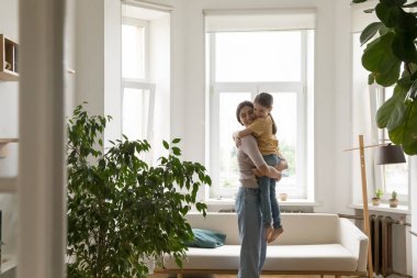 Güçlü bir bağ. Sevgi dolu gülümseyen anne oturma odasında durur kucağında küçük kızı kucağında tutar duygusal kucaklaşmayla tatlı kavuşma anını kutlar ayrı düştükten sonra barışı sağlar.