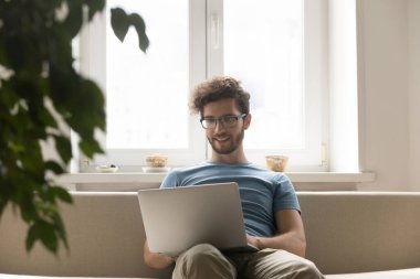 Odaklandım ama rahatladım. Gülümseyen genç adam başarılı serbest çalışan uzaktan çalışan oturma odasındaki rahat kanepe üzerinde not defteri kullanın internet sitesi içeriği sohbeti için internet üzerinden görevleri yönetin