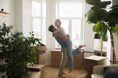 İlk ev satın alma başarısı. Neşeli genç evli çift gülüyor. Yeni daire mülkiyetini kutluyorlar. Oturma odasındaki kiracıları kutluyorlar.