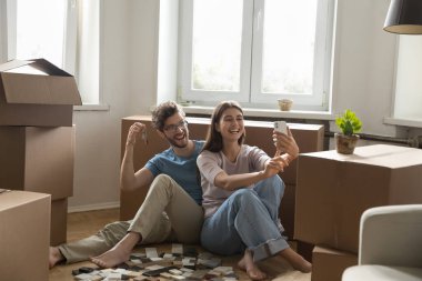 İlk kez ev sahipleri selfie çekiyor. Neşeli genç eşler yeni bir daire almanın başarısını paylaşıyorlar. Mutlu eş kutuların arasında görüntülü konuşma yapıyor. Telefonda canlı yayında. Mutluluktan uçan koca elinde anahtar tutarken kendini çek.