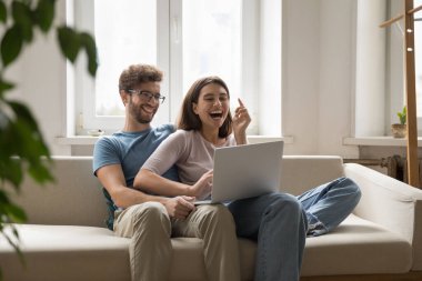 Çevrimiçi sevinç anı. Aşırı neşeli, birbirine aşık genç çift kanepede kucaklaşmanın keyfini çıkarıyorlar. Not defteri kullanarak komik komedi filmleri aboneliği izleyip internet mimleri üzerinden samimi kahkahalar atıyorlar.