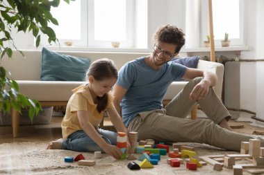Hayal gücü şehri. Şirin küçük kız yerde oynuyor. İnşaat setinden parlak ahşap blok kasabası yaratıyor. Güler yüzlü babanın desteğiyle.