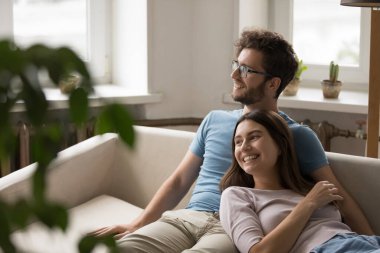 Birlikte sessiz rüyalar. Gülümseyen eş, kanepeye uzanmış sevgili kocasına yaslanıyor. Hayalperest genç çift mesafeye bakar. Paylaşılmış yolculuk planı hayal et. Yeni bir ev satın al.