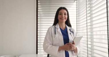 İçerde poz veren neşeli genç bayan doktor dijital tablet tutuyor, kameraya bakıyor, gülümsüyor. Mutlu Latin doktor kadın, pratisyen, cerrah, sağlık hizmeti profesyonel portresi