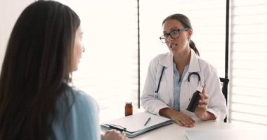 Gözlüklü neşeli, genç, Kafkasyalı GPS doktoru grip tedavisi için hasta kadına şurup, ilaç, gıda takviyesi, sağlıklı yaşam için vitaminler, başarılı bir rehabilitasyon öneriyor.