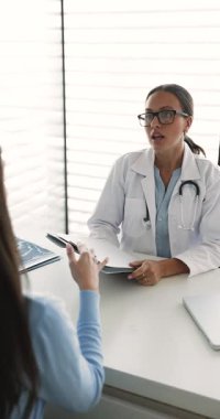 Şık gözlüklü ve laboratuvar önlüklü genç bayan doktor ofiste kadınlara danışmanlık yapıyor, sağlık şikayetlerini dinliyor, hastalarla konuşuyor, teşhisi ve terapiyi açıklıyor. Dikey çekim