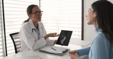 Neşeli kadın doktor ve hasta tablet üzerinde röntgen çekimleri, iyileşme, kırık kemikler üzerine rehabilitasyon, gülmek, eğlenmek hakkında tartışıyorlar. Travma cerrahına danışan genç bir kadın.