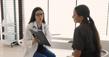 Gözlüklü genç kadın doktor hastaya tıbbi raporlar gösteriyor, teşhisi açıklıyor, tedavi için sağlık tavsiyeleri veriyor, hastane ofisinde danışmanlık yapıyor.