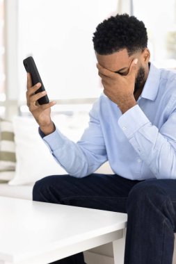 Dijital felaket. Şok olmuş genç adam koltukta oturur telefon kılıfını tutar kötü haberle boğulmuş avuç içi mesajla çevrimiçi piyangoda para kaybeder kötü amaçlı yazılımın kurbanı olur.