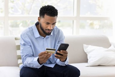 İnternet bankası. Odaklanmış gen z erkek oturma odasındaki koltukta oturur akıllı telefon kartı tutar çevrimiçi satın almayı onaylar nakit para gönderme yoluyla para gönderilir web bankacılık uygulaması yoluyla ödeme sağlar. Boşluğu kopyala