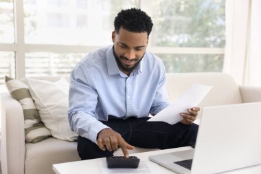 Finansal görevlere güven. Gülümseyen genç adam zoomer, defter uygulaması ile online ödeme yapmadan önce bütçe hesaplama işi kontrol masası giderlerini gözden geçirmek için hesap makinesi kullanın.