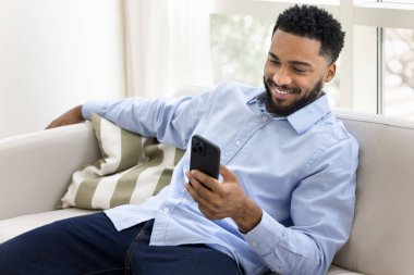 Gevşeme modu aktif. Mutlu genel z hipster adam konforlu kanepe üzerinde uzanır modern cep telefonuyla mesajlaşır arkadaşlarıyla eğlenceli videolar paylaşır sosyal medyada oyun oynar