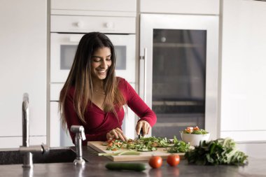 Ev yemeği hobisi. Mutfak mutfağında yetenekli bir aşçı olan mutlu genç kadın taze malzemeler kullanarak doğal sebze salatası pişirme sanatının keyfini çıkarıyor.