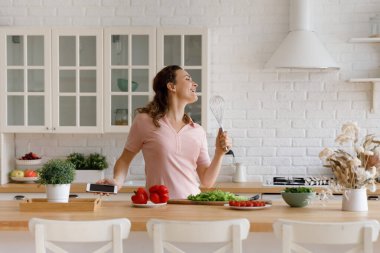 Mutlu aşçı kız mutfakta eğleniyor, akşam yemeği yapıyor, müzik eşliğinde dans ediyor, sebzelerle çırpıda şarkı söylüyor, akıllı telefondan şarkılar dinliyor.