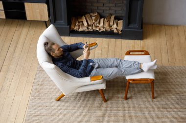 Rahatlamış genç milenyum akıllı telefon kullanıcısı oturma odasındaki koltukta dinleniyor, cep telefonunda sanal ekommerce uygulaması kullanıyor online alışveriş için, internette geziniyor, sosyal medya evde. Üst görünüm