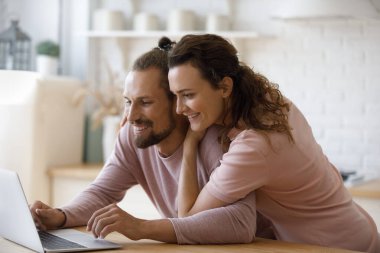 Mutlu genç aile, dizüstü bilgisayarlarını kullanarak ev mutfağında film, dizi izliyor, video görüşmesi yapıyor, bilgisayarları paylaşıyor, internetten alışveriş yapıyor, gülümsüyor, gülüyor.