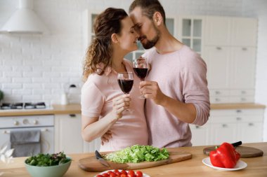 Sevgili milenyum buluşmaları, sevgililer günü, yıldönümü nedeniyle mutfakta kırmızı şarap içen evli çiftler, romantik akşam yemeği için salata hazırlamak, kapalı gözlerle öpüşmek, kadeh kaldırmak.