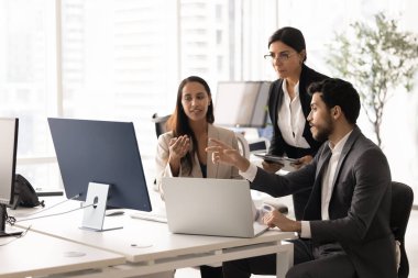 Beyin fırtınası yapmak, çevrimiçi ürün geliştirme, internet satış sonuçları, bilgisayar monitörüne işaret etmek ve konuşmak için dizüstü bilgisayarın başında toplanan üç genç ve yaşlı iş arkadaşı.