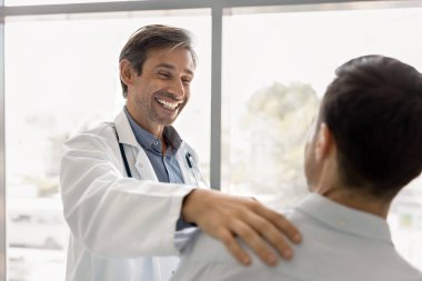 İyileşmenin mutluluğunu paylaş. Neşeli kahkahalar atan olgun doktor, sağlıklı erkek hastaların omuz omuza, sempati ve sempati ile, sağlık gelişiminden memnun, etkili tedavi sonuçları.