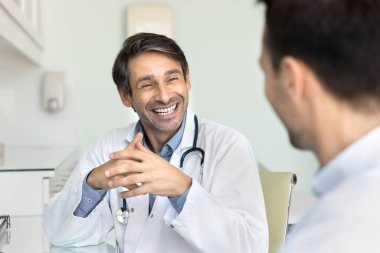 Arkadaş canlısı doktor ve hasta ilişkisi. Neşeli, pozitif erkek doktor klinikteki masada oturup aktif dinleyerek ziyaretçilere destek oluyor ve tıbbi sağlık muayenesinde tedavi detaylarını tartışıyorlar.