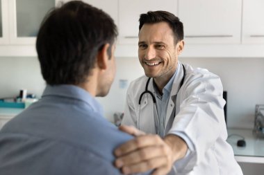 Güvenilir bir doktorun destek eli. Gülümseyen nazik tıbbi uzman orta yaşlı bir adamın elini omzuna koydu. Hastayı teşhisin üstesinden gelmeye teşvik etti. Pozitif terapi sonuçlarına olan güvenini dile getirdi.